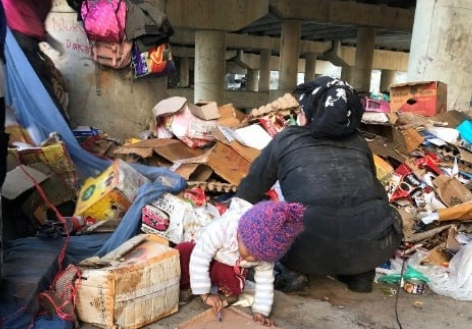 woman with a young toddler picking through a large waste pile.