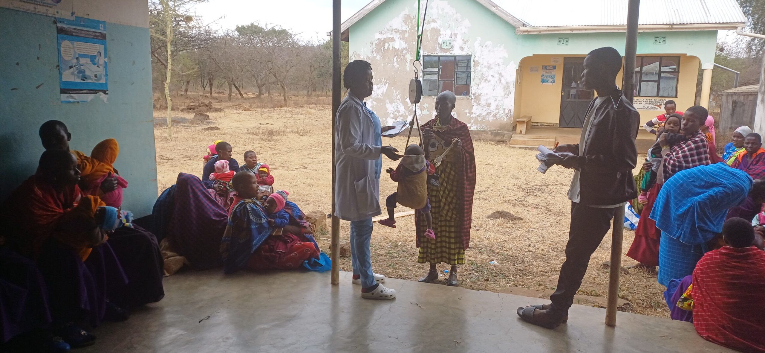 1000664034 Massai women and children in an outdoor healthcare facility, infant being weighed