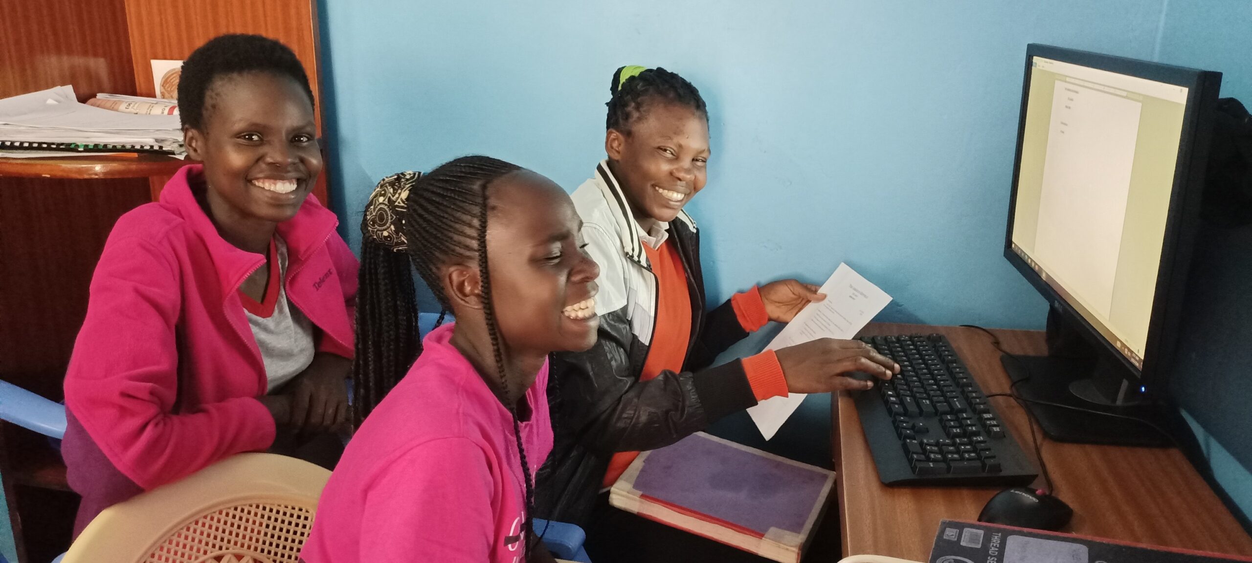 kids smiling, sitting at a desk in front of a desk top computer