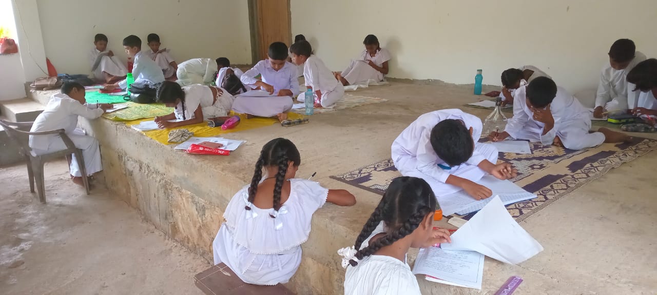 school kids sitting on a concrete or dirt flooring doing school work