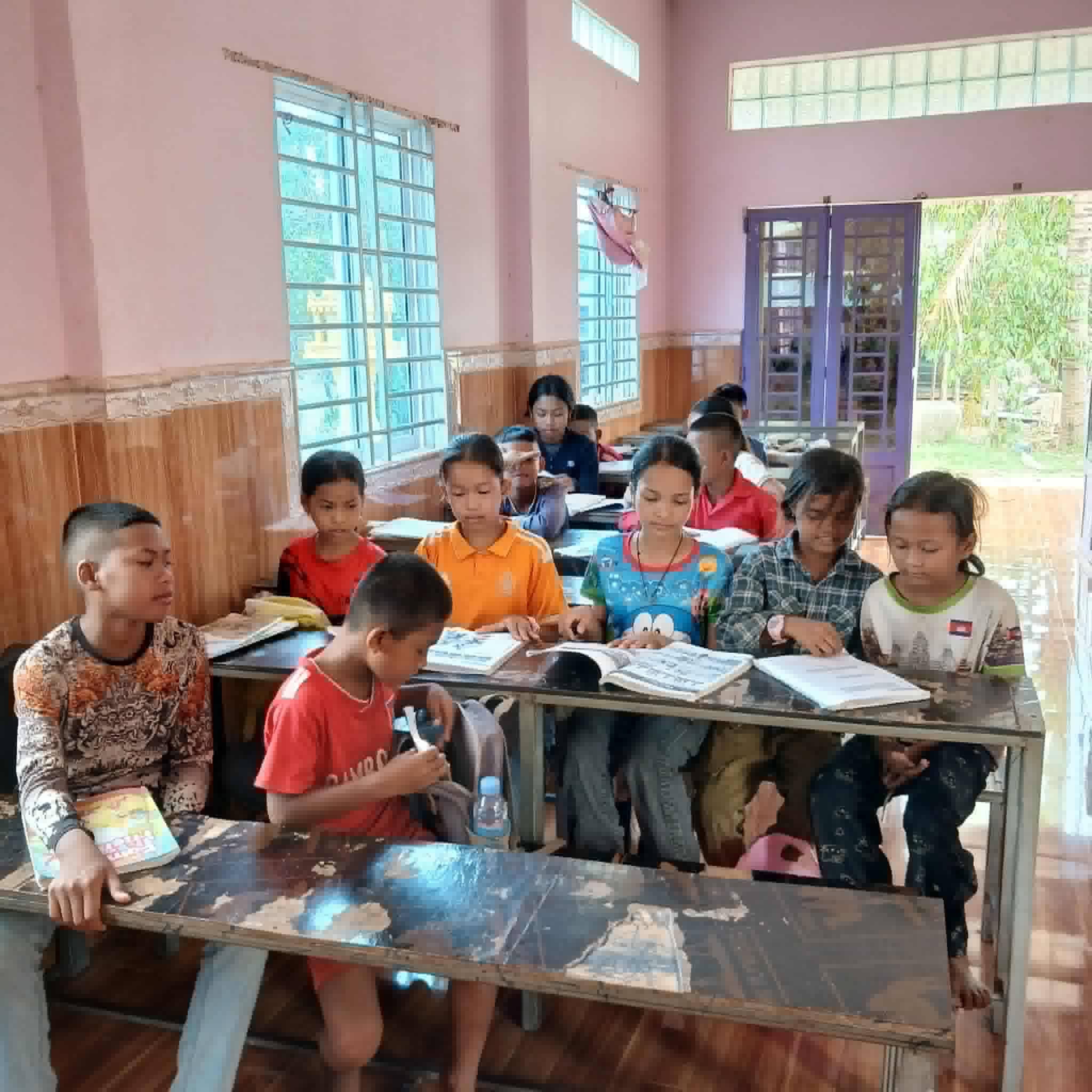 children in a classroom sitting at wooden tables next to eachother