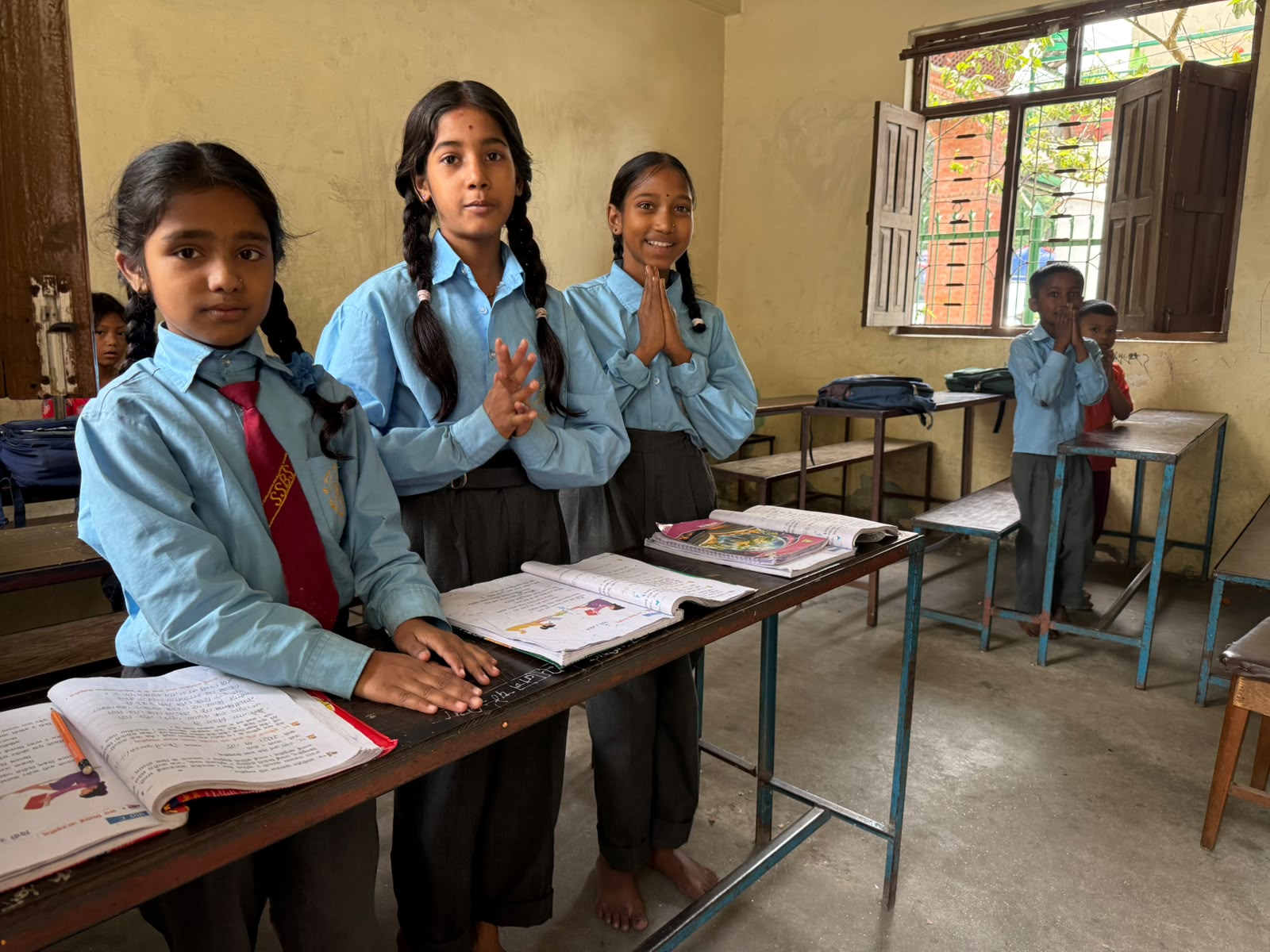school children in uniform standing at their desks with prayer hands
